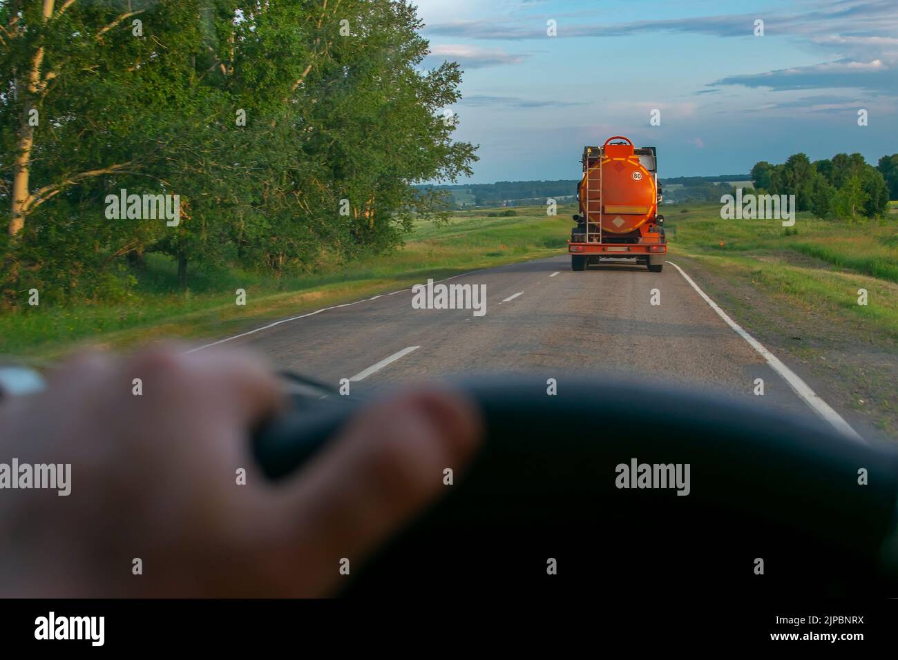 vista di una petroliera con serbatoio arancione che trasporta merci infiammabili su una strada di campagna sullo sfondo di un conducente che sta guidando dietro un autocarro Foto Stock