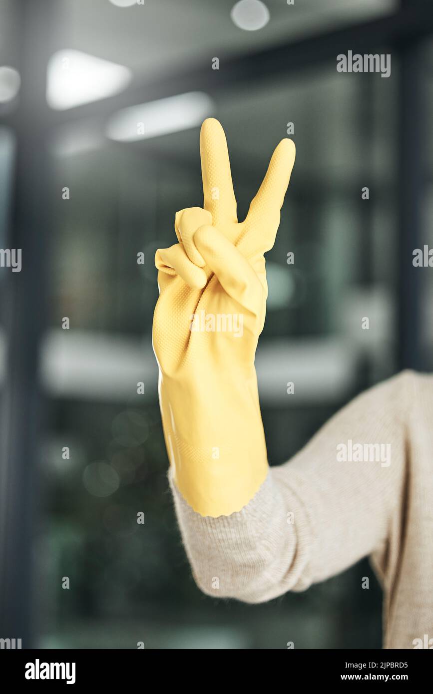 Segno di pace, spensierato e gesto della mano mentre pulisce, facendo i lavori domestici e di lavoro da solo a casa. Primo piano delle dita di un conteggio più pulito, che esprime Foto Stock