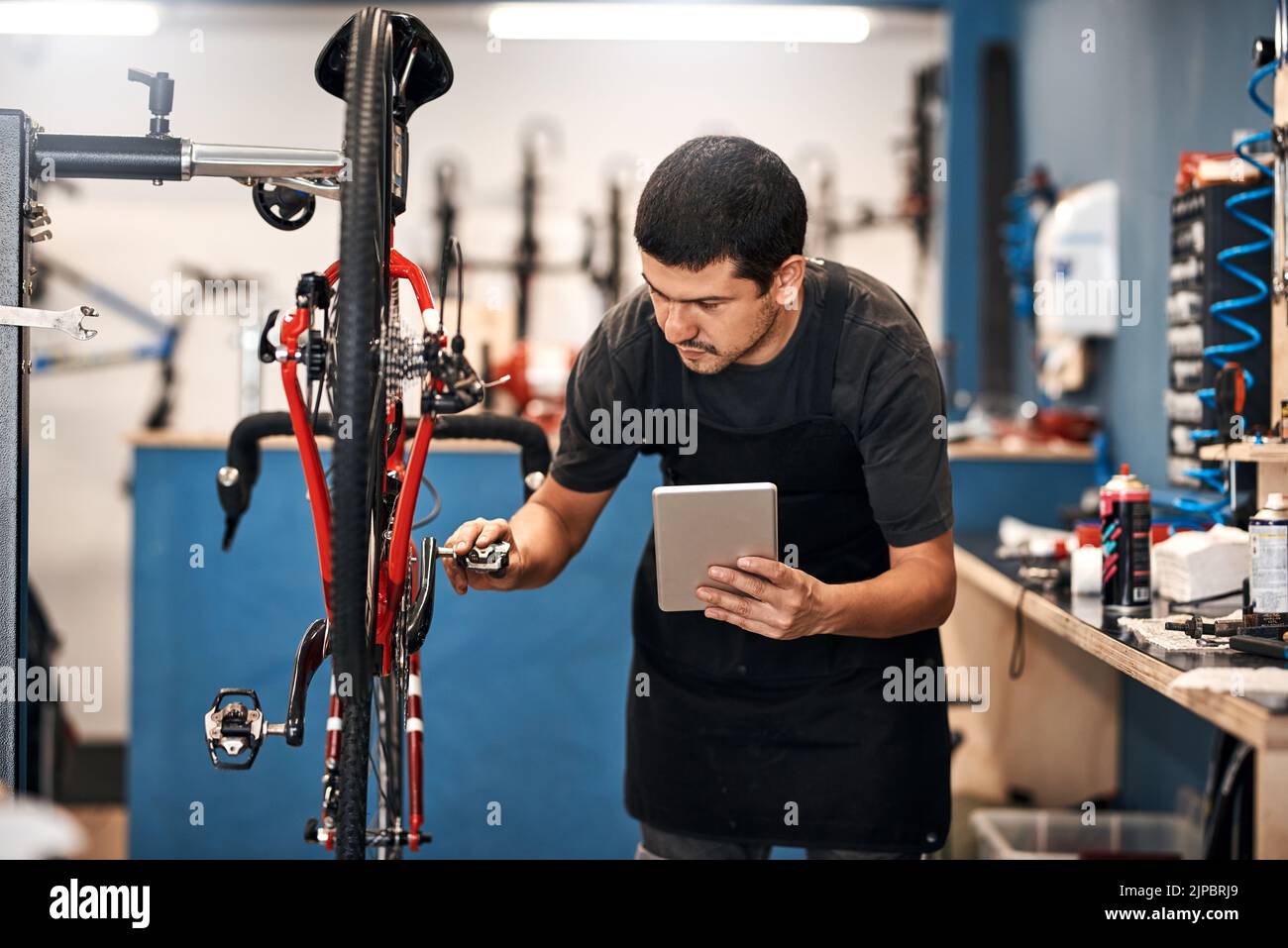 Un'app per tutto, anche per la riparazione di biciclette. Un uomo che usa un tablet digitale in un negozio di riparazione di biciclette. Foto Stock