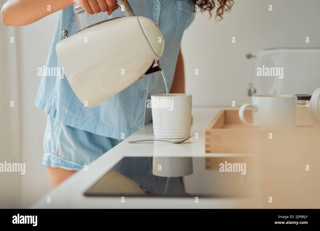 Mattina, caffè prima colazione e le mani femminili versano acqua in tazza dal retro bollitore in cucina a casa. Donna in pigiama preparare il tè o fare un Foto Stock