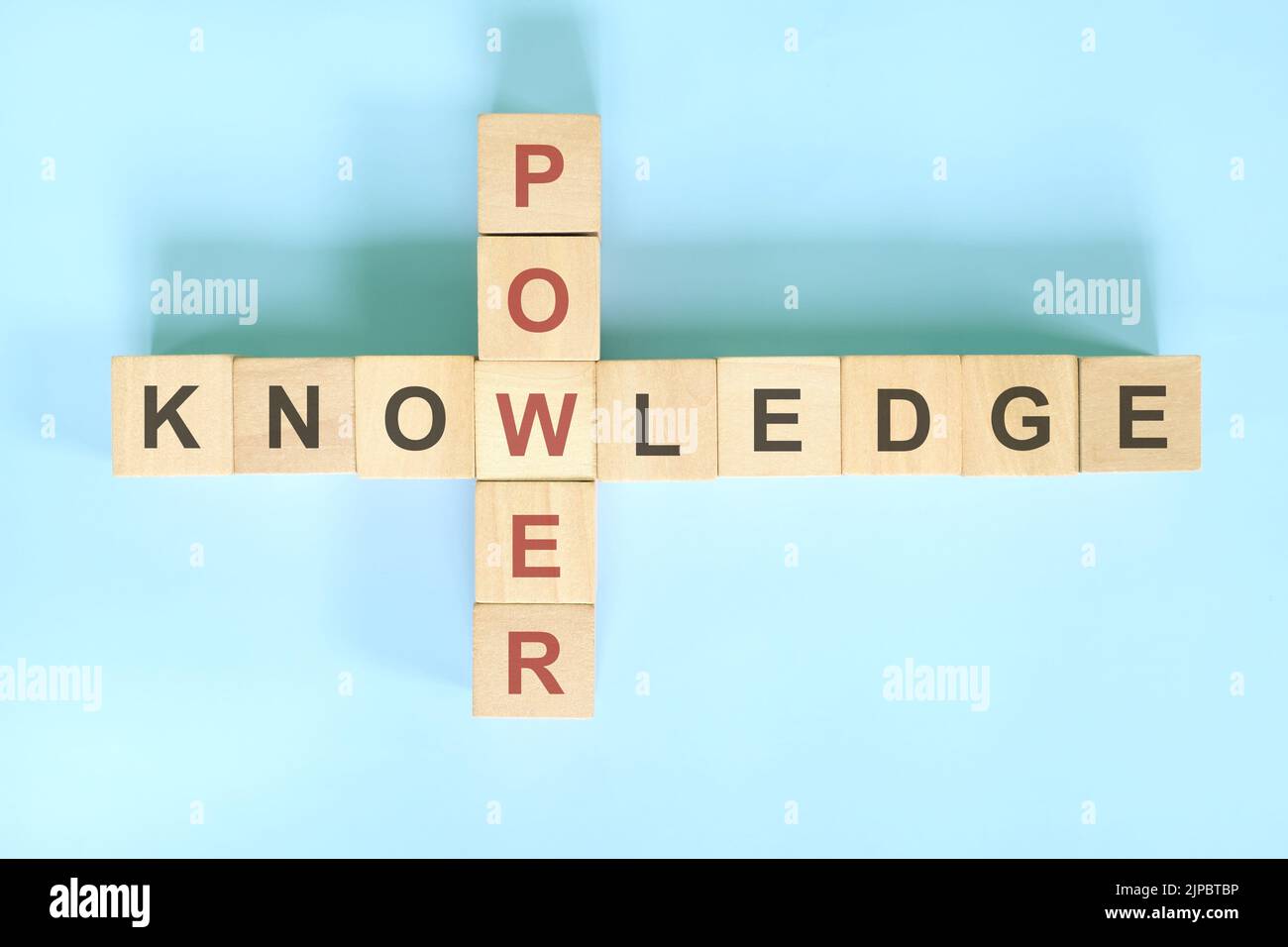 La conoscenza è concetto di potere. Legno blocco crossword puzzle piatto giacitura su sfondo blu. Foto Stock