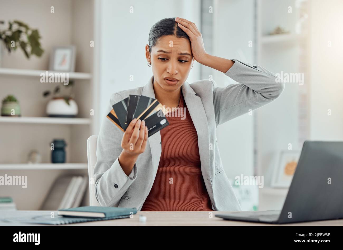 Stress finanziario, preoccupata e frustrata donna che tiene le carte di credito in mano alla sua scrivania. Imprenditoria preoccupata per le decisioni economiche, credito Foto Stock