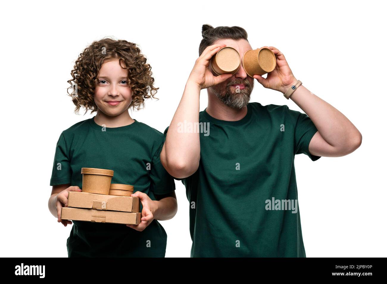 Divertente Eco-attivisti Famiglia indossare T-shirt verde in White Studio. La bambina femminile e l'uomo bello tiene scatole di cartone e tazze di zuppa monouso. Era Foto Stock