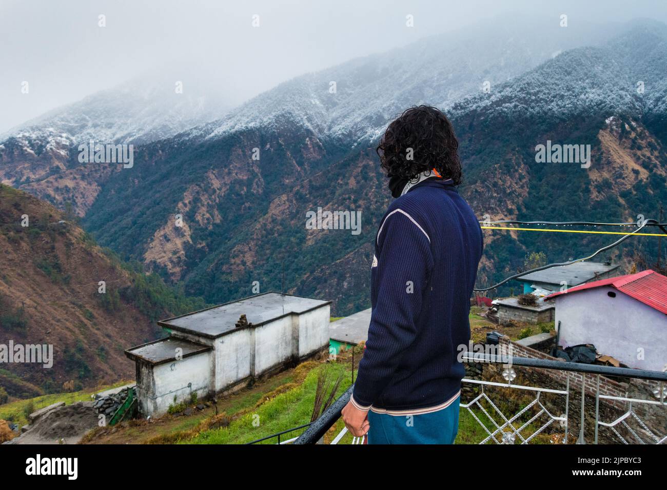 Uttarakhand. India. 23rd Jan2022.A uomo in piedi sul tetto di una casa di villaggio con montagne innevate di himalaya nel quartiere di Okhimath di Cha Foto Stock