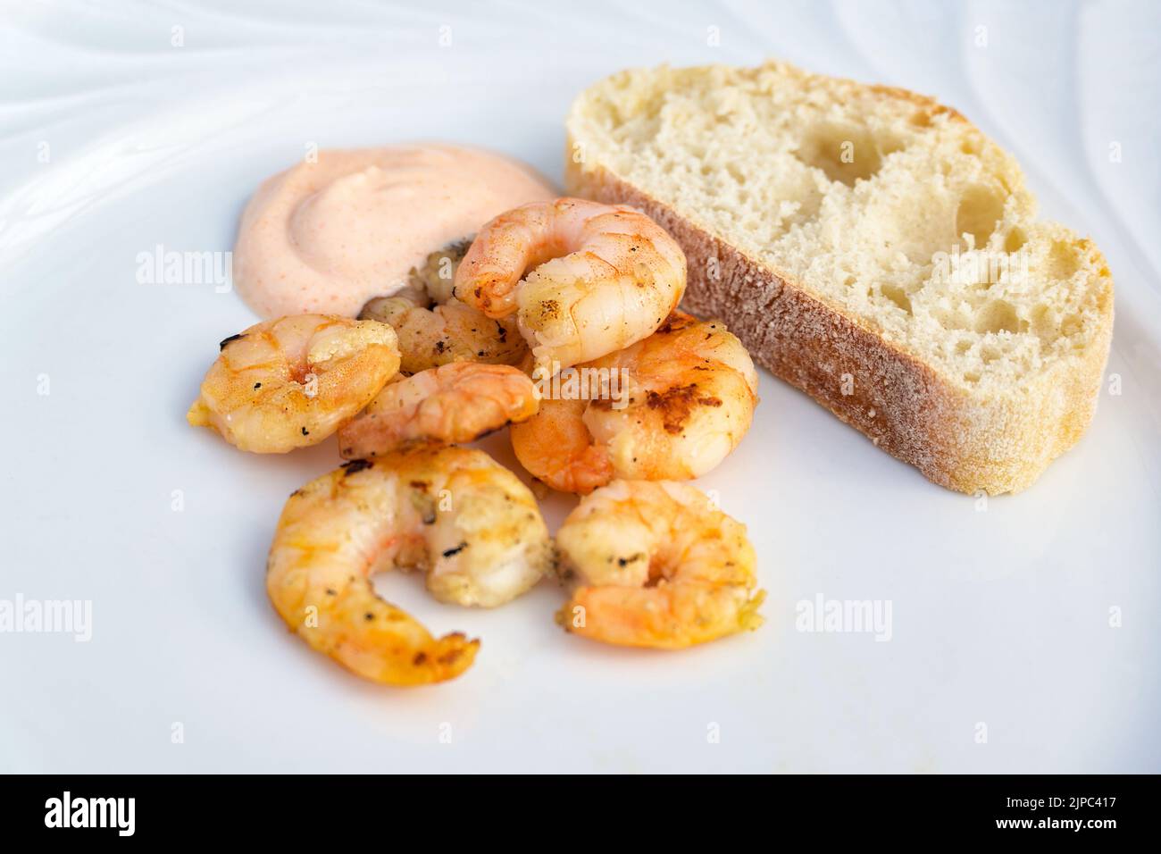 Gamberetti o gamberi arrosto con salsa cocktail e pane su un piatto bianco come antipasto in uno spazio per la copia della cena, focus selezionato, profondità molto stretta di fuoco Foto Stock