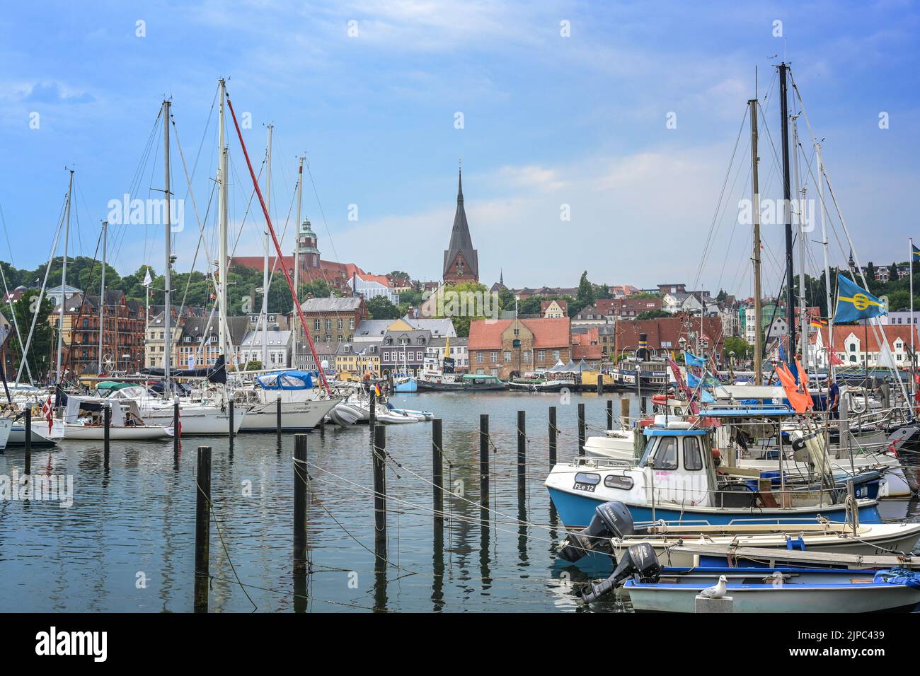 Flensburg, Germania, 25 luglio 2022: Città vecchia con chiesa di San Mariano dietro il porto yacht con barche a vela, al fiordo sul Baltico Foto Stock