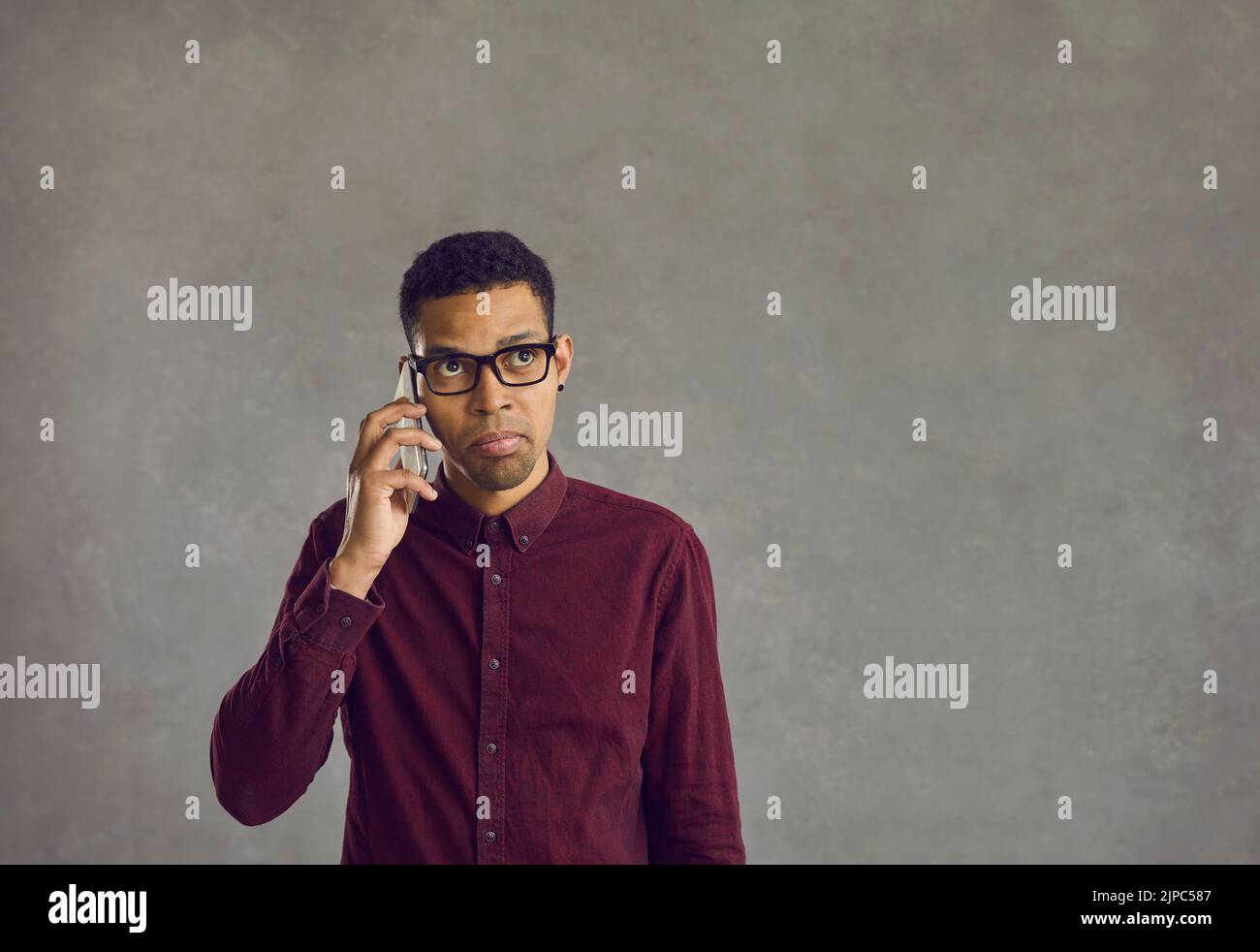 Giovane uomo nero confuso che tiene il telefono cellulare, effettua una chiamata e aspetta una risposta Foto Stock