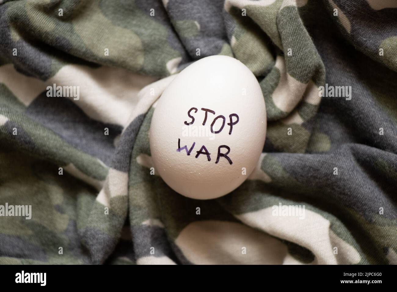 Uovo di pollo bianco con l'iscrizione stop guerra che si trova su una mimetizzazione militare uniforme, cibo e guerra in Ucraina Foto Stock