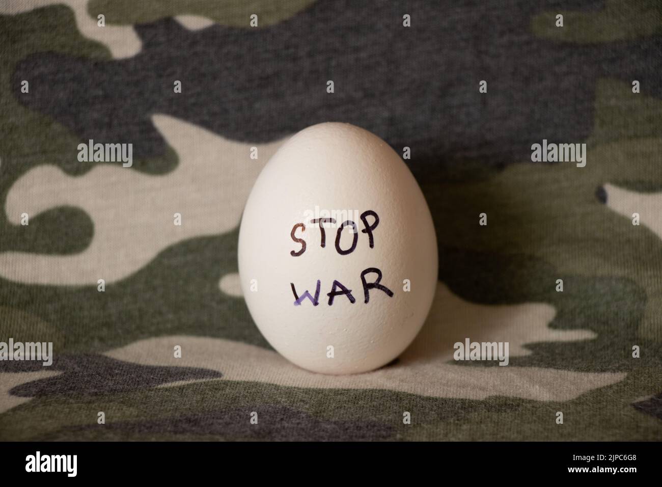 Uovo di pollo bianco con l'iscrizione stop guerra che si trova su una mimetizzazione militare uniforme, cibo e guerra in Ucraina Foto Stock