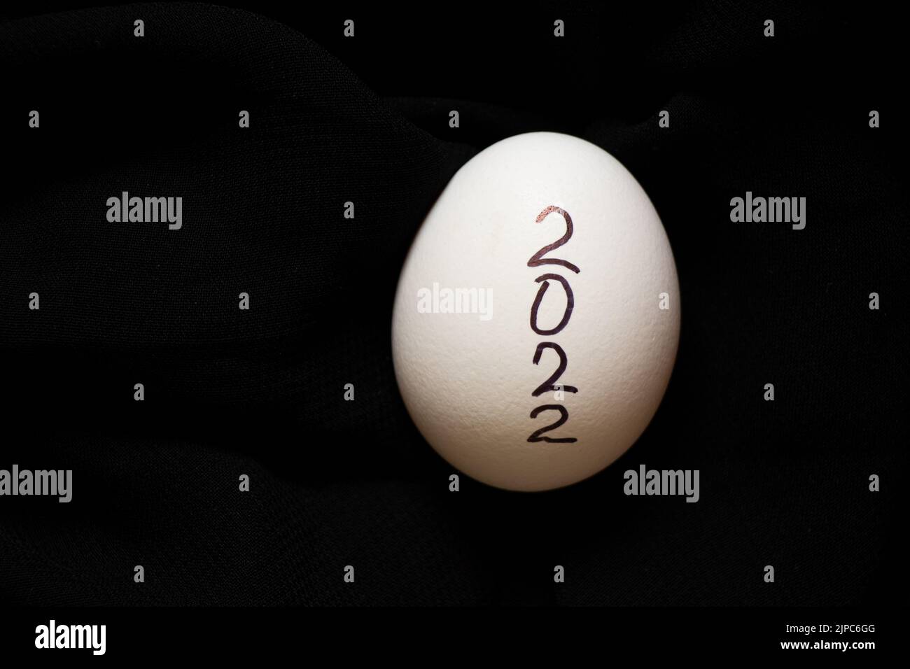 Uovo di pollo bianco su sfondo nero con testo scritto 2022, pasqua e cultura nel nuovo anno, cibo Foto Stock