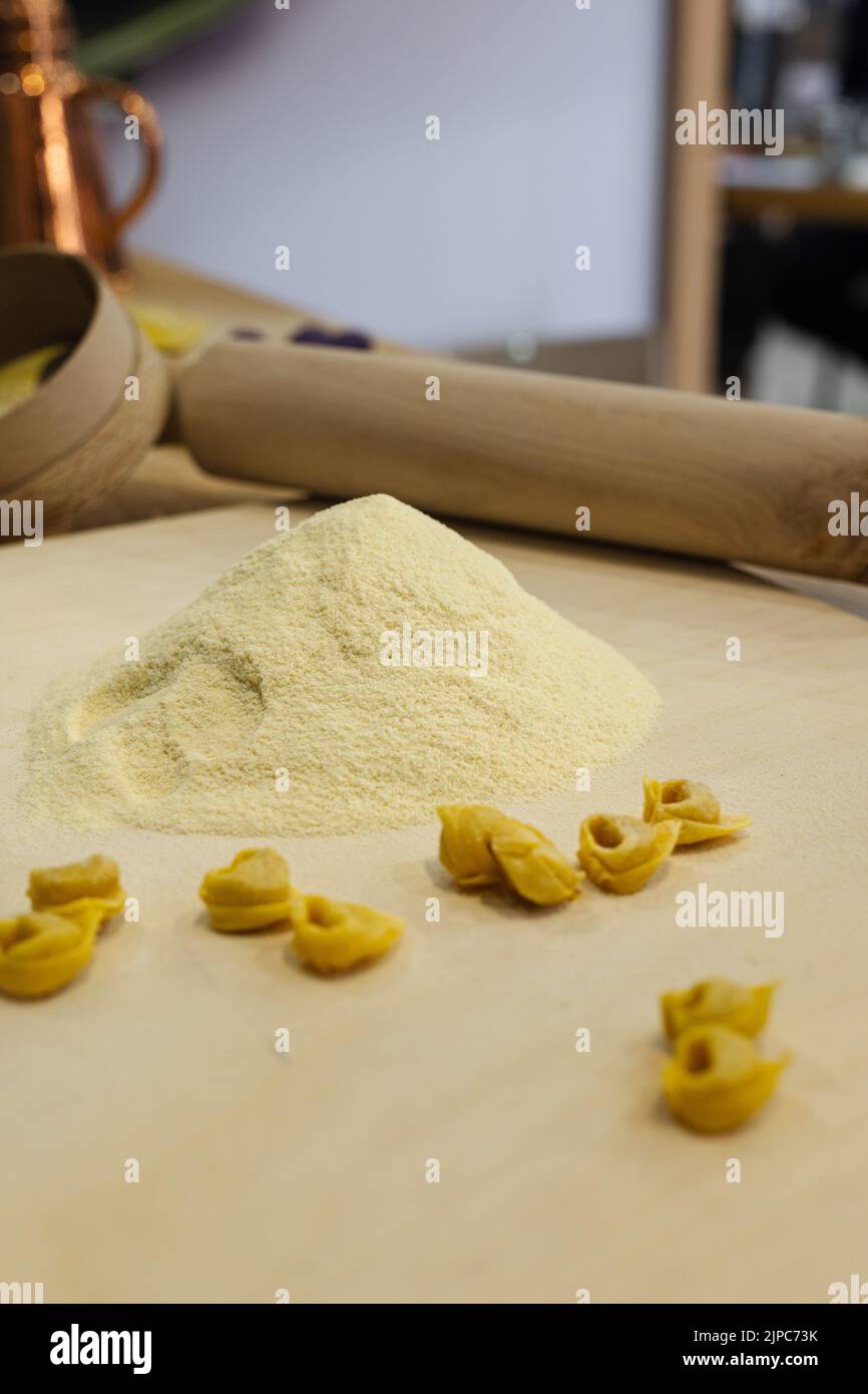 Tortellini crudi appena fatti su tavola di legno e un matterello e farina sullo sfondo. Foto Stock