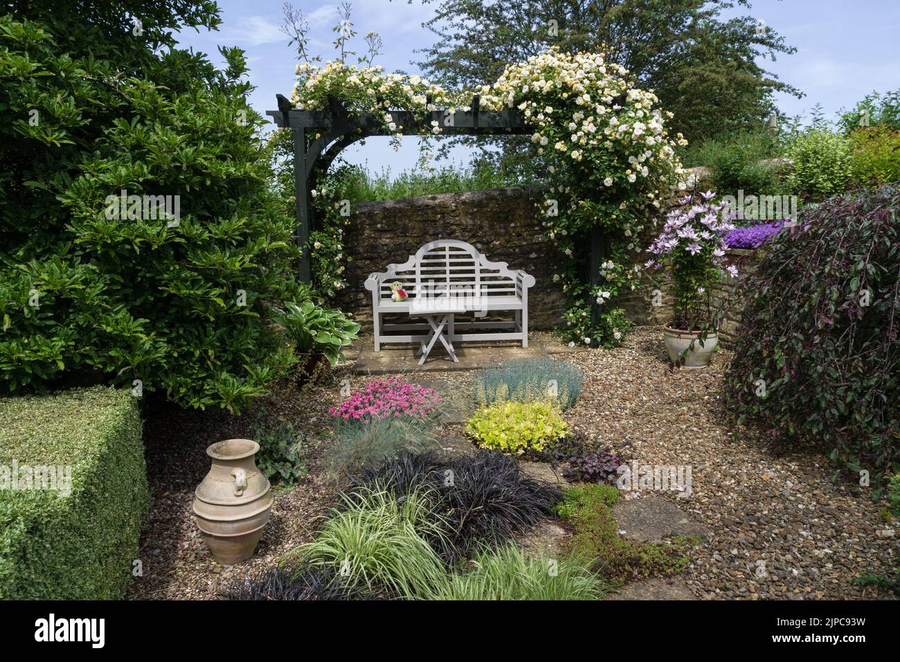 Un giardino inglese in estate, Gayton, Northamptonshire, UK; arbour, panca bianca e piante che crescono in ghiaia. Foto Stock