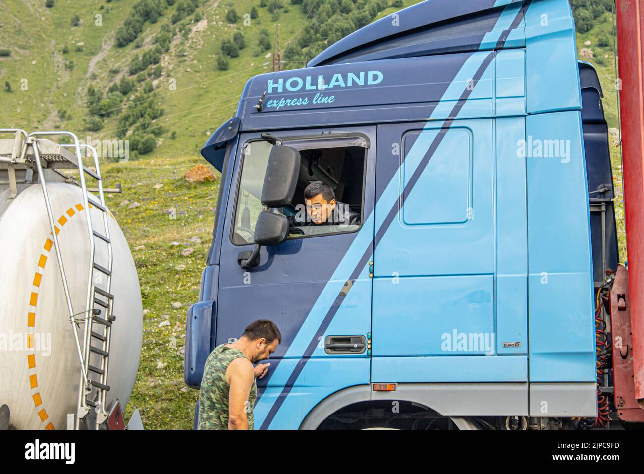 In una lunga coda di camion in un ingorgo stradale vicino al confine russo in Georgia, un conducente si inclina fuori dal suo taxi per parlare con un altro conducente Foto Stock