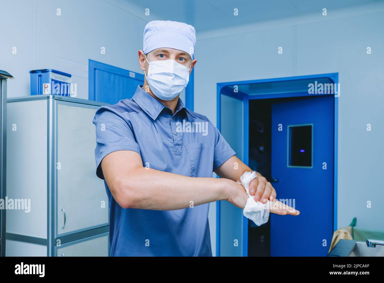 Un chirurgo maschio disinfetta le mani prima dell'intervento chirurgico. Un medico in una maschera chirurgica e uniforme strofinare le mani con un panno antisettico. Disinfezione delle mani prima dell'intervento chirurgico. Foto Stock
