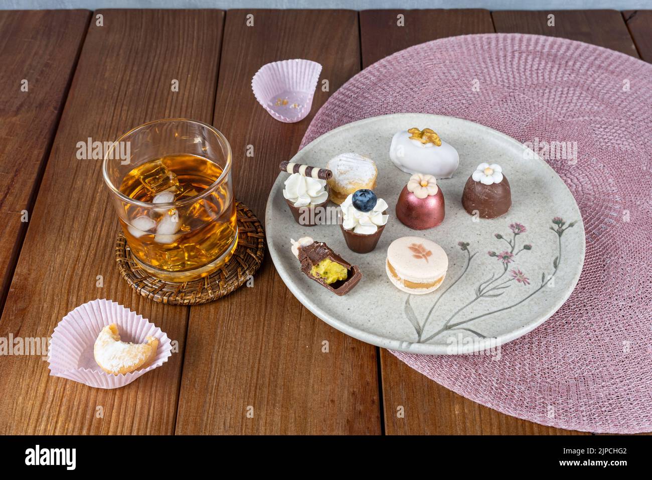 Piccolo bicchiere di cioccolato con panna montata e gelato ai mirtilli accanto ad altri dolci e bicchiere di whiskey. Foto Stock