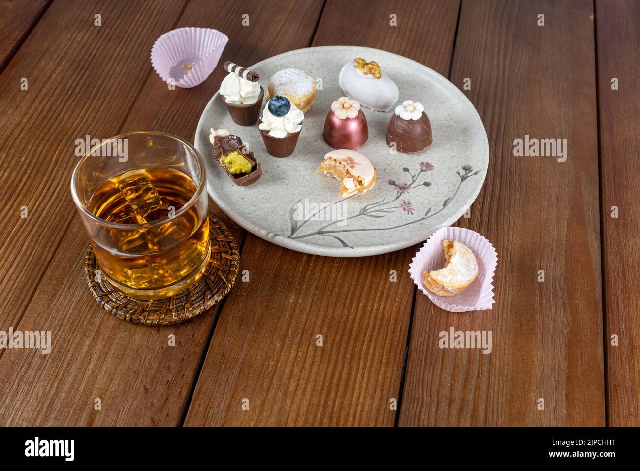 Amalgamare il macaron accanto a un piccolo bicchiere di cioccolato con crema di pistacchio, tartufi, cameo di noce e bicchiere di whiskey. Foto Stock