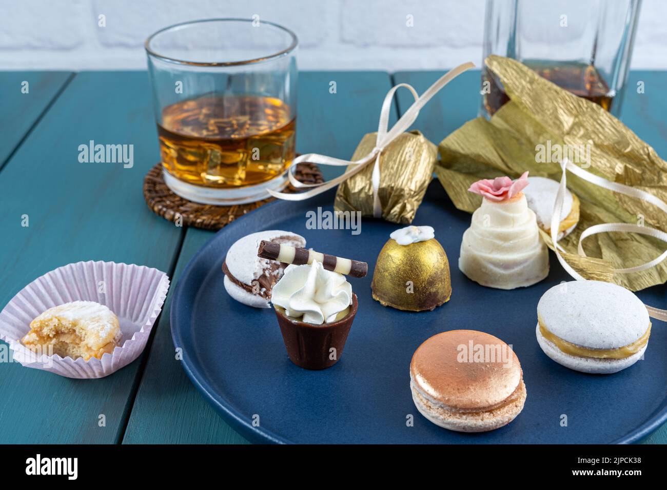 Piccolo bicchiere di cioccolato con panna montata, accanto a macaron, cameo di noce, tartufo, bottiglia e bicchiere di whisky. Foto Stock