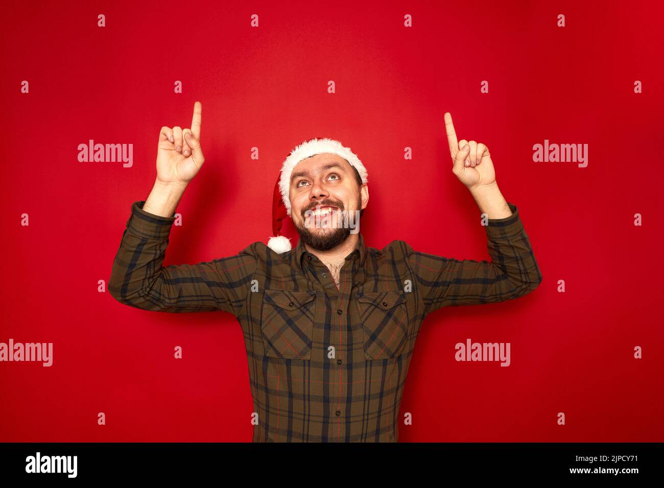 Ritratto di uomo sorridente in abiti casual cappello di Natale puntando le sue dita indice in uno spazio vuoto Foto Stock