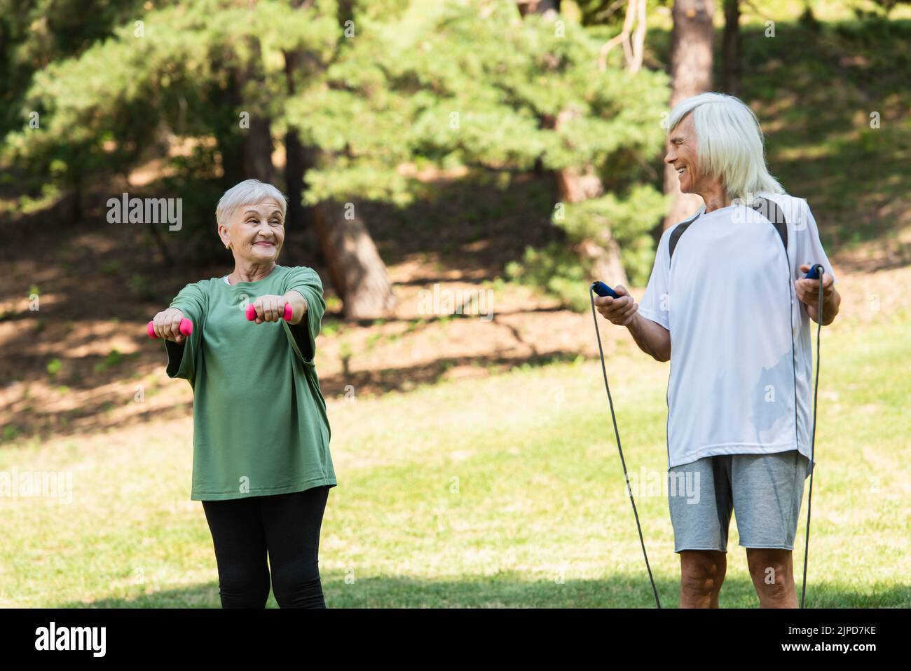 allegra coppia anziana in abbigliamento sportivo con attrezzature sportive nel parco verde Foto Stock