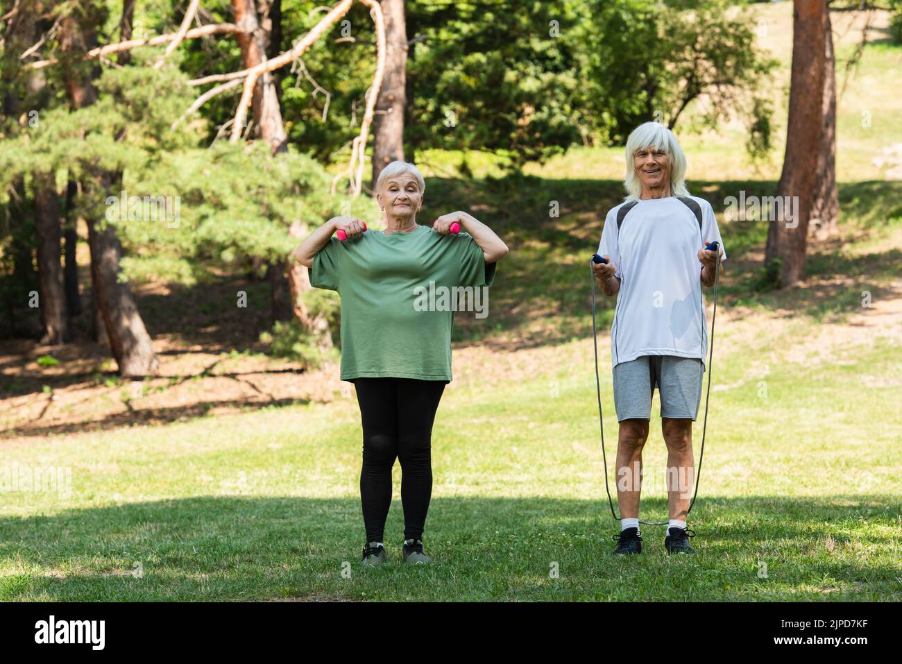 lunghezza intera di coppia anziana allegra in sportswear esercitandosi con l'apparecchiatura sportiva nel parco verde Foto Stock