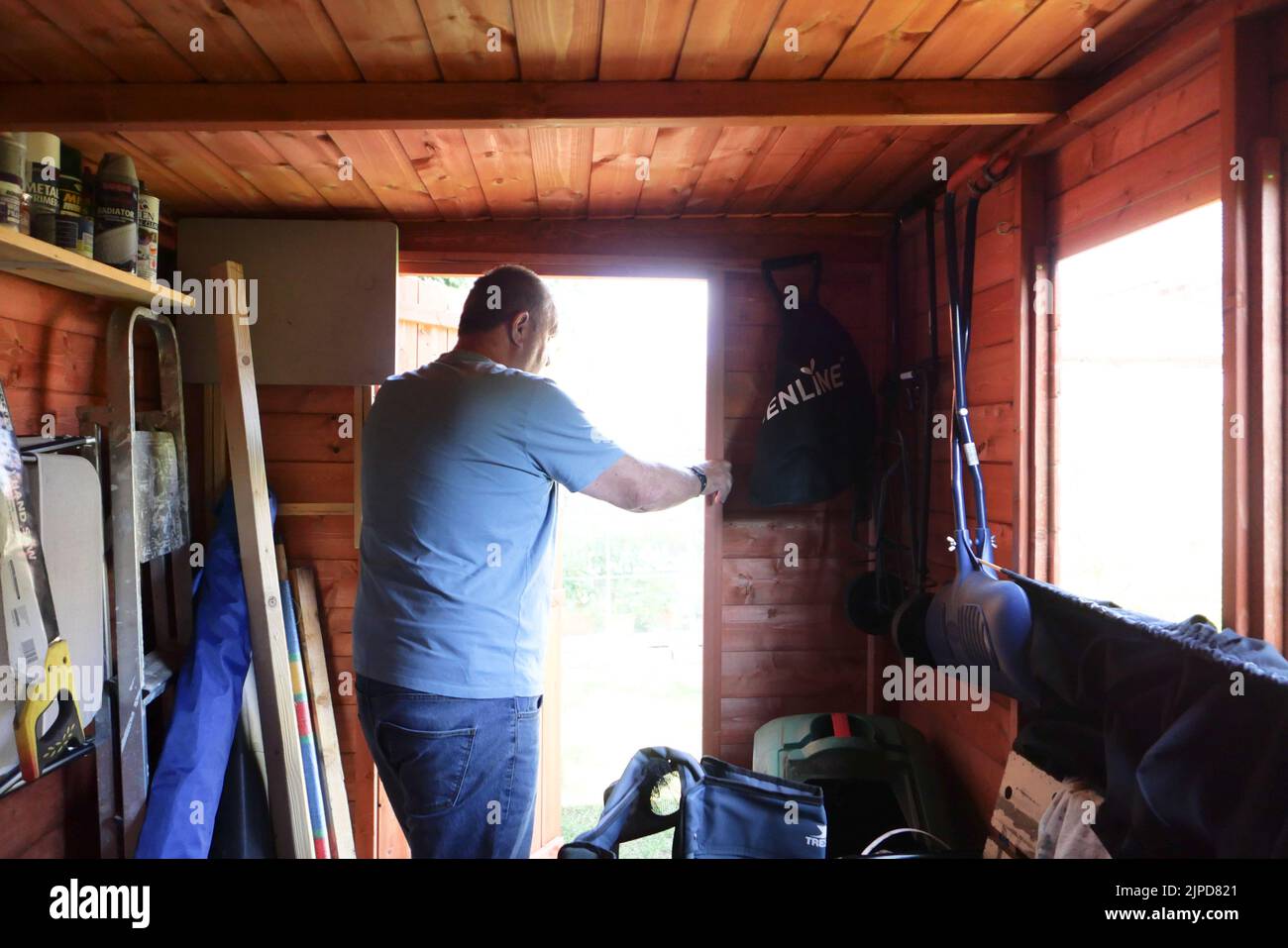 Uomo anziano in t-shirt in piedi in un vano porta. Ripresa dall'interno. Foto Stock