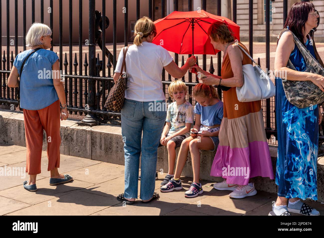 Due bambini sono schermati dal sole con un ombrello fuori da Buckingham Palace il giorno più caldo mai registrato, Londra, Regno Unito Foto Stock