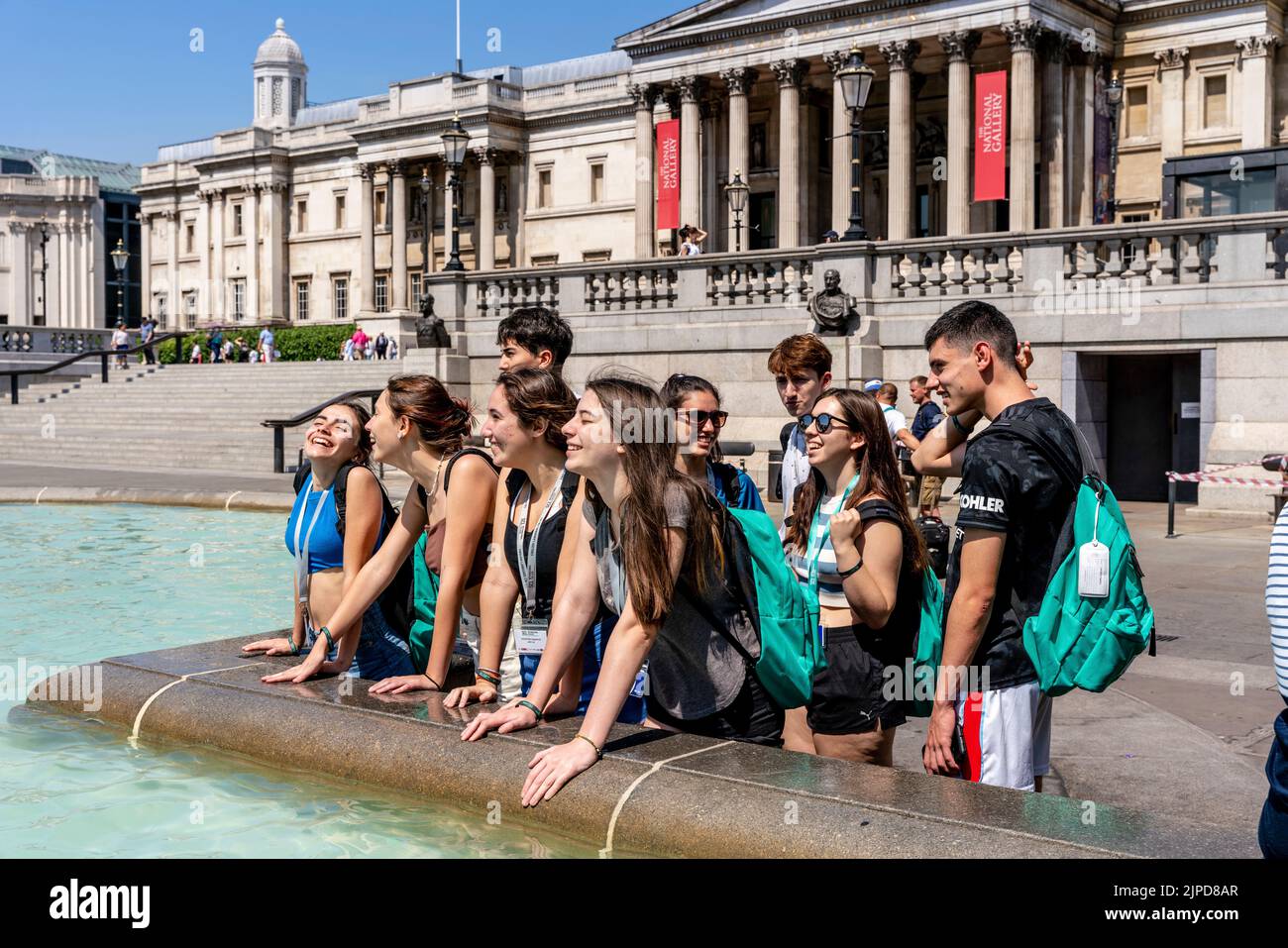 Un gruppo di giovani turisti si raffreddano nella Spray of the Fountains a Trafalgar Square il giorno più caldo mai registrato nella capitale, Londra, Regno Unito Foto Stock