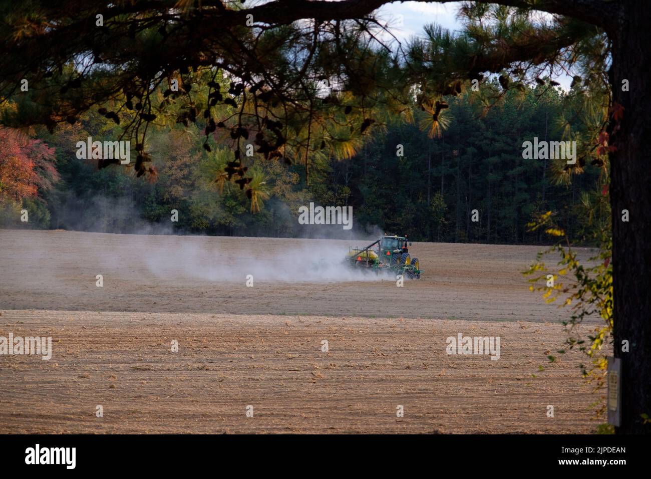 Ampio colpo di trattore che tira un disco su un terreno coltivato, mescolando la polvere. Foto Stock