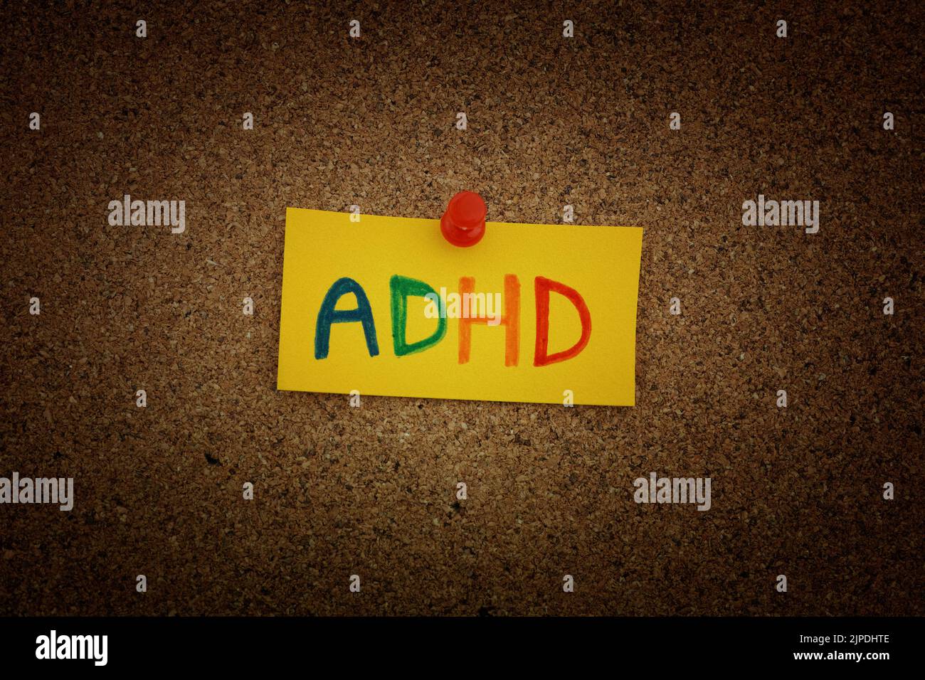 Una nota di carta gialla con l'abbreviazione ADHD su di essa fissata a una tavola di sughero. Primo piano. L'ADHD è un disturbo da deficit di attenzione e iperattività. Foto Stock