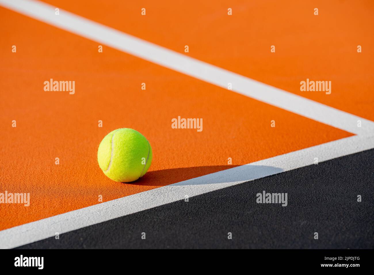 Palla da tennis gialla nel nuovo campo da tennis arancione all'aperto con baseline bianca e nero fuori limite. Foto Stock