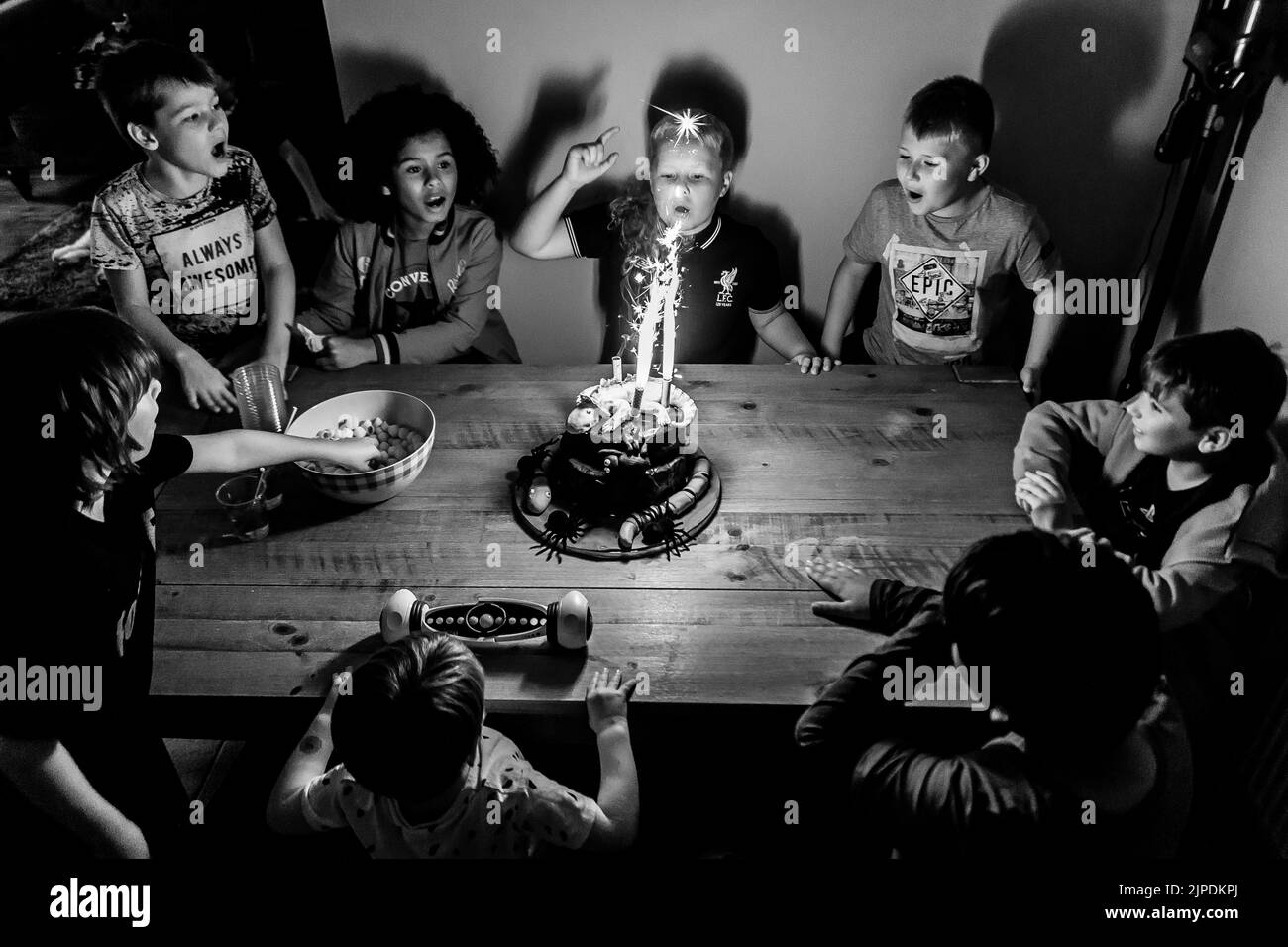 Un'immagine monocromatica di una festa di compleanno dei bambini con molti ragazzi seduti attorno ad un tavolo con una torta di compleanno al centro con gli scintillanti. Foto Stock