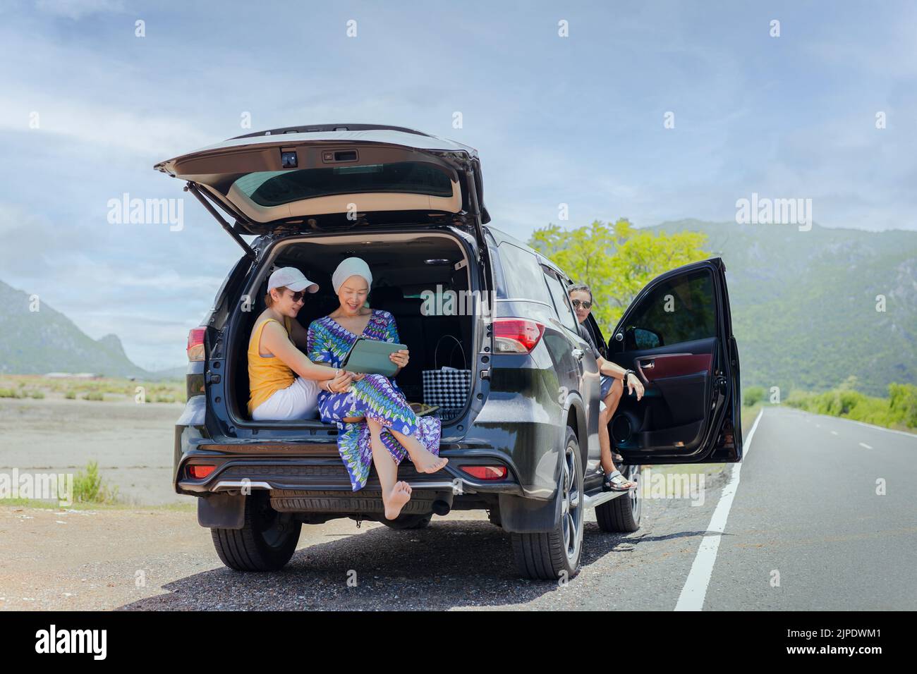 Gruppo di amici seduti nel bagagliaio aperto di un'auto nera che guarda il tablet. Foto Stock