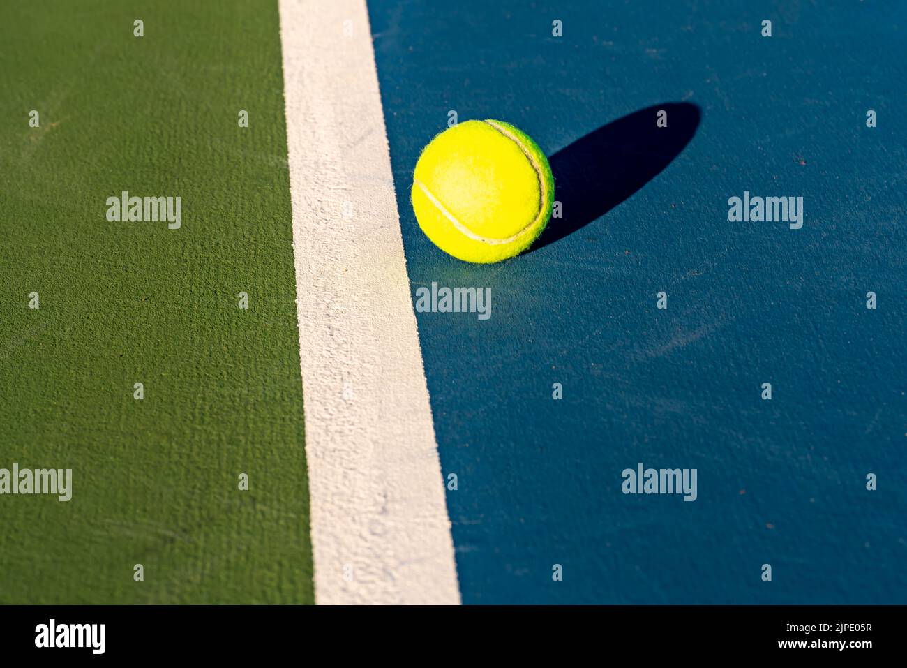 Palla da tennis gialla vicino alla linea di base su un nuovo campo da tennis blu con verde fuori limite. Foto Stock