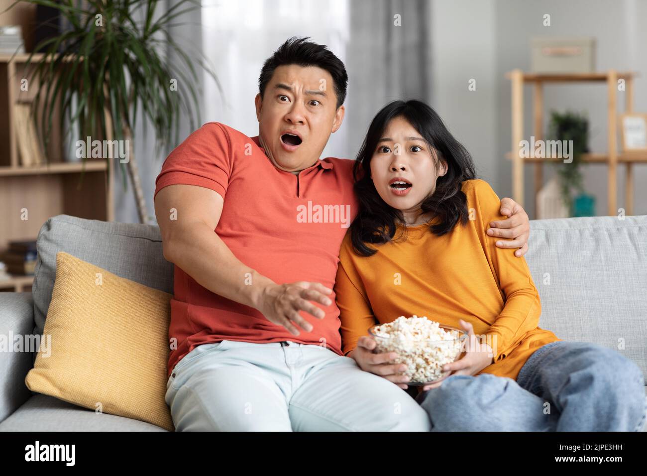Uomo e donna coreani entusiasti che guardano film spaventosi a casa Foto Stock