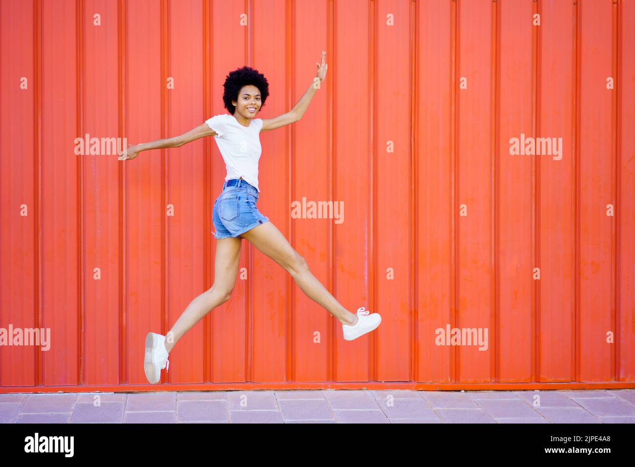 Content donna nera che salta vicino al muro rosso Foto Stock