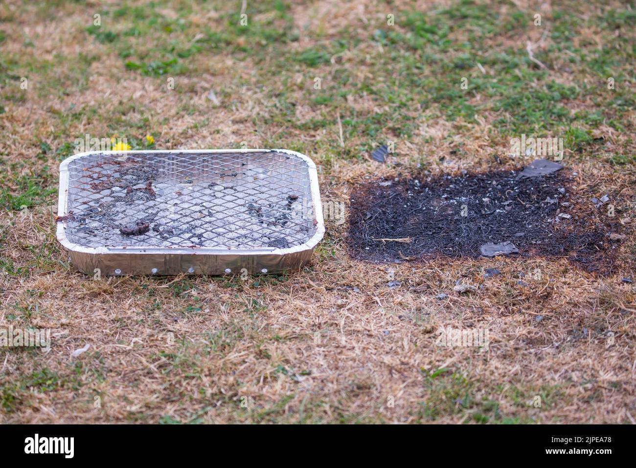 Primo piano del barbecue usa e getta lasciato come spazzatura nel punto di bellezza della campagna del Regno Unito - pericolo di incendio pericoloso con erba bruciata sotto in onda di calore! Foto Stock