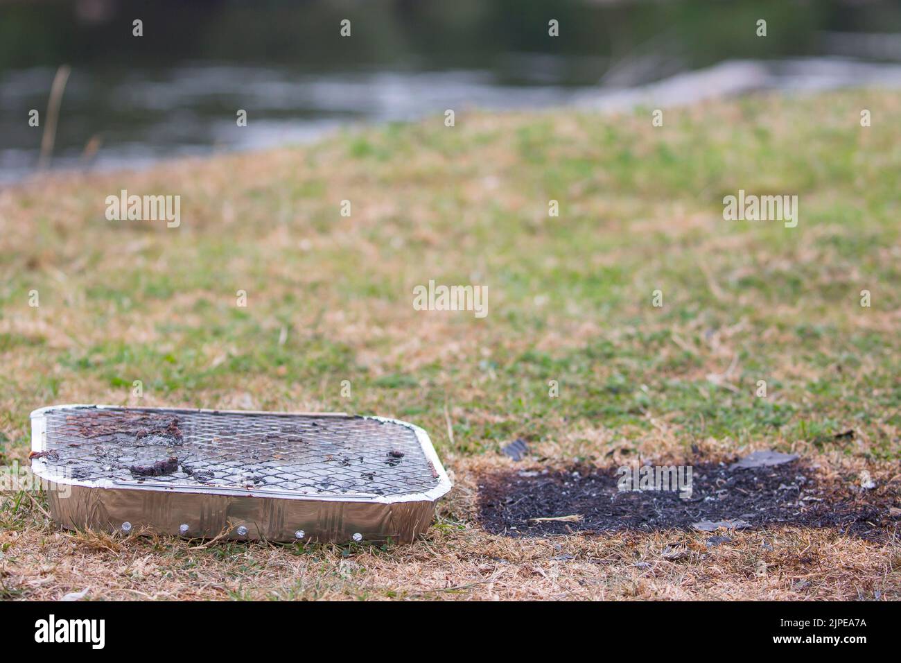 Primo piano del barbecue usa e getta lasciato come spazzatura nel punto di bellezza della campagna del Regno Unito - pericolo di incendio pericoloso con erba bruciata sotto in onda di calore! Foto Stock