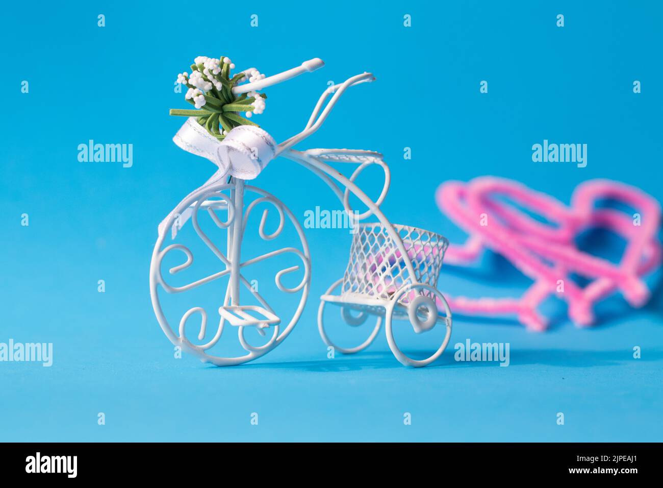 Bicicletta decorativa, personaggio di bicicletta in filo sottile bianco isolato su sfondo blu. Cuori rosa sul retro. Lasciare, metafora di separazione, allegoria. Foto Stock