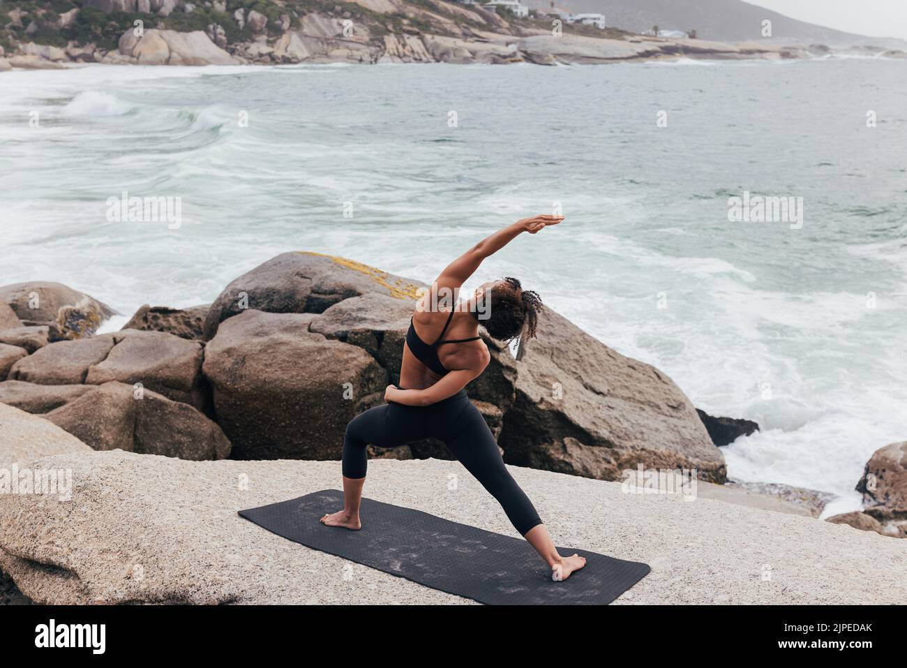 Donna sana praticando Utthita Parsvakonasana yoga posa. Donna che si esercita vicino ad un oceano. Foto Stock