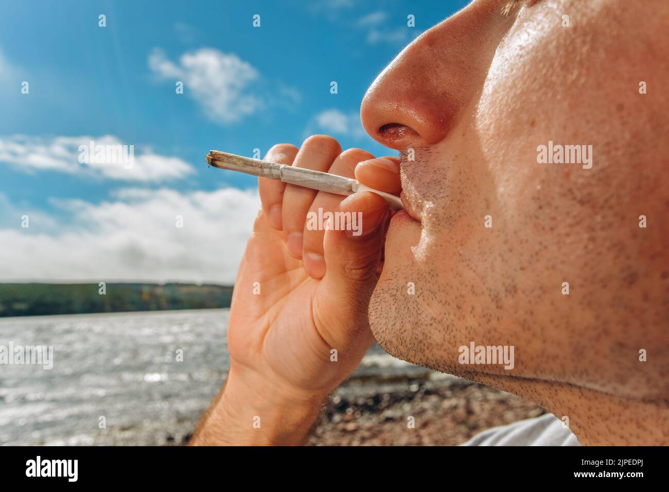 Particolare di un uomo che fuma una marijuana o un'erbaccia che si rilassa sulla riva di un lago. Foto Stock