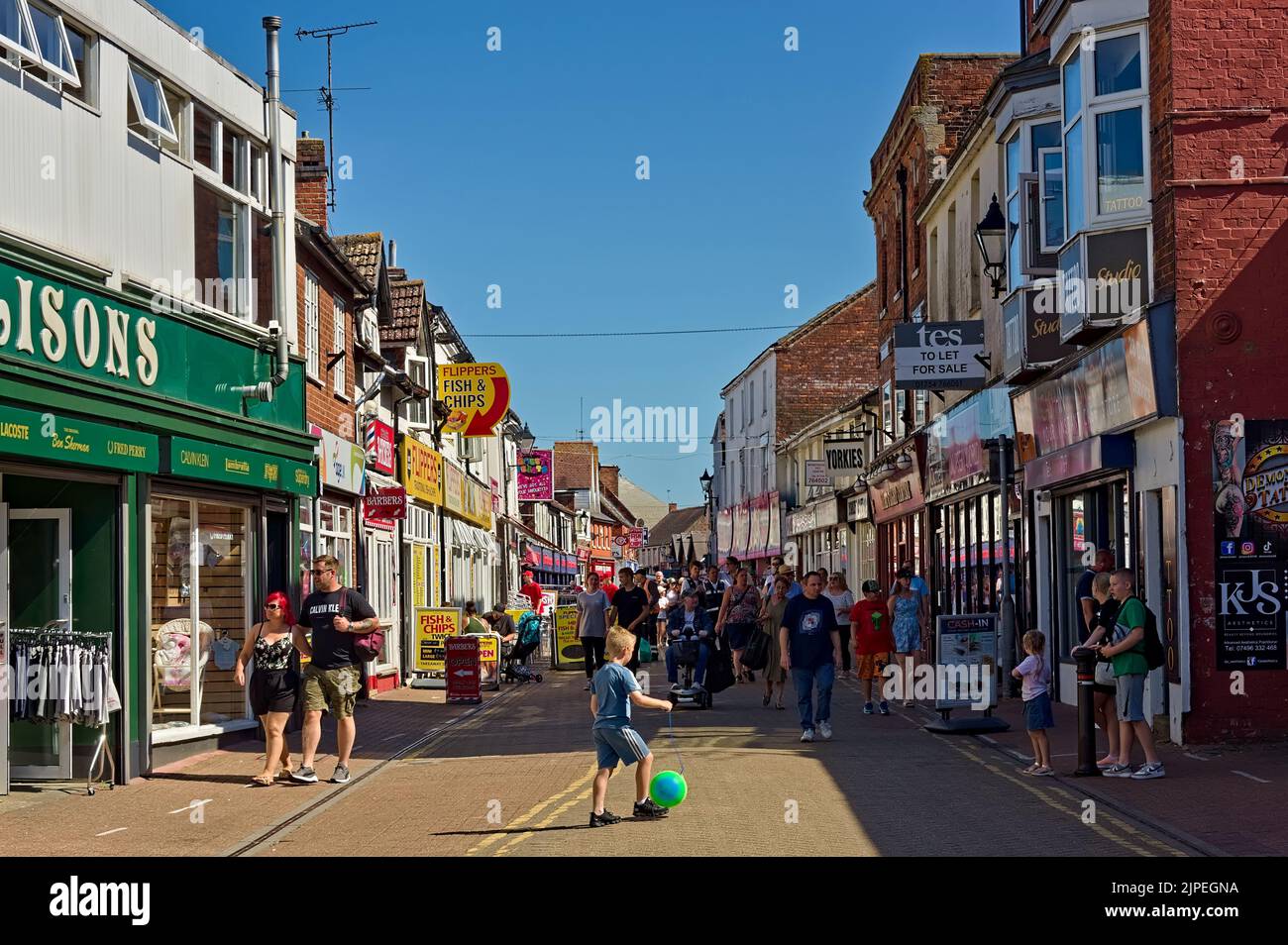 Folle di persone sulla High Street, affettuosamente note come "vicolo del chip" a Skegness, con un bambino che gioca a palla in primo piano Foto Stock