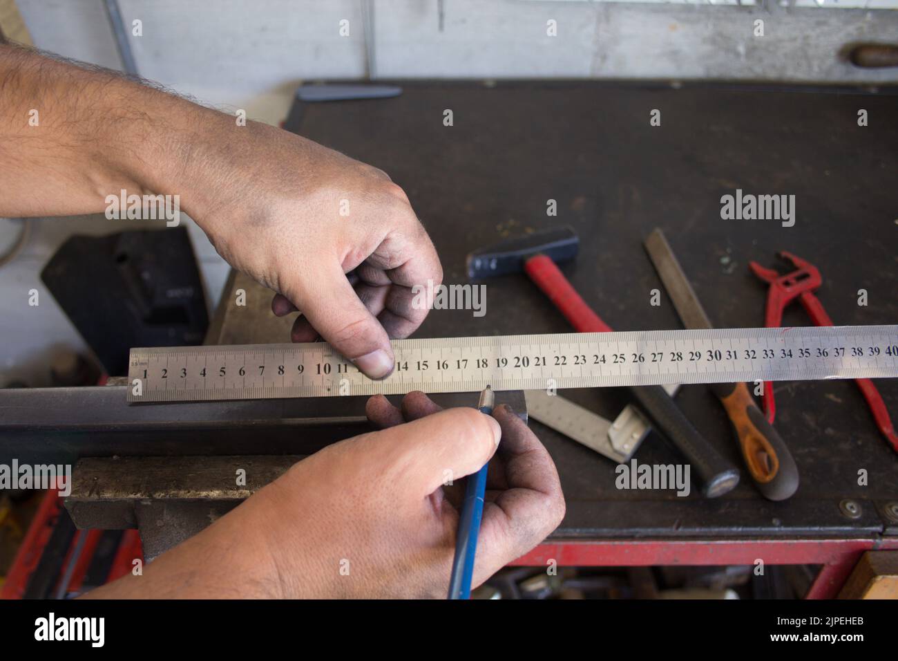 Mani sporche di un fabbro che prende misure con righello e matita su un pezzo di ferro da tagliare e lavorare. Contesto con strumenti del commercio Foto Stock