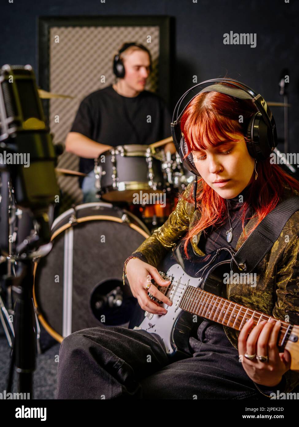 Giovane donna rossa che suona chitarra elettrica e un batterista maschile in uno studio di registrazione. Foto Stock