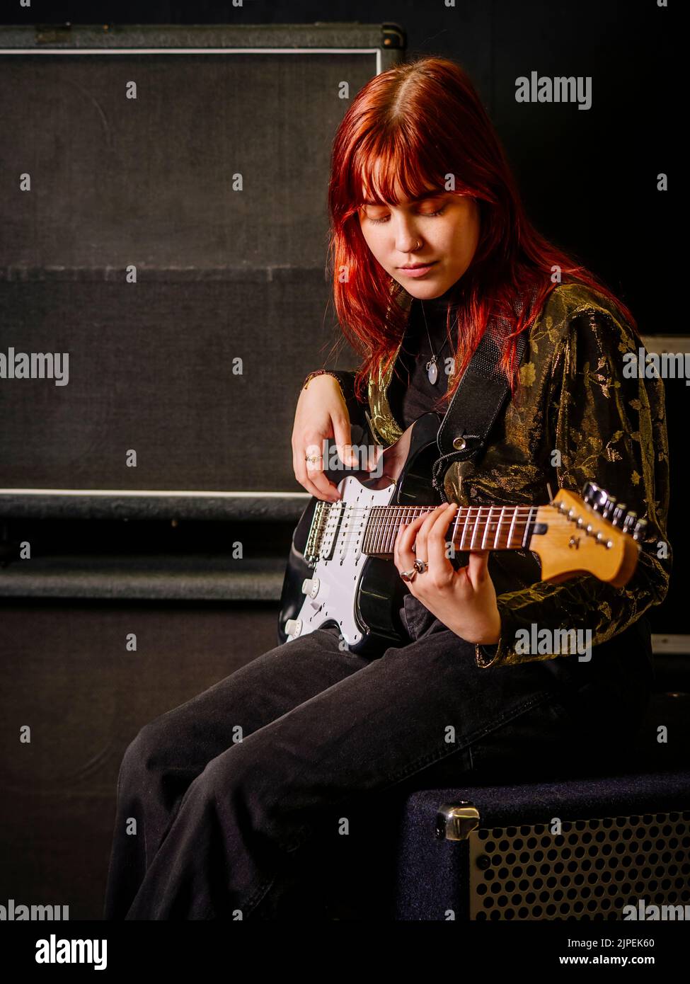 Giovane donna rossa che suona la chitarra elettrica di fronte a grandi casse. Foto Stock