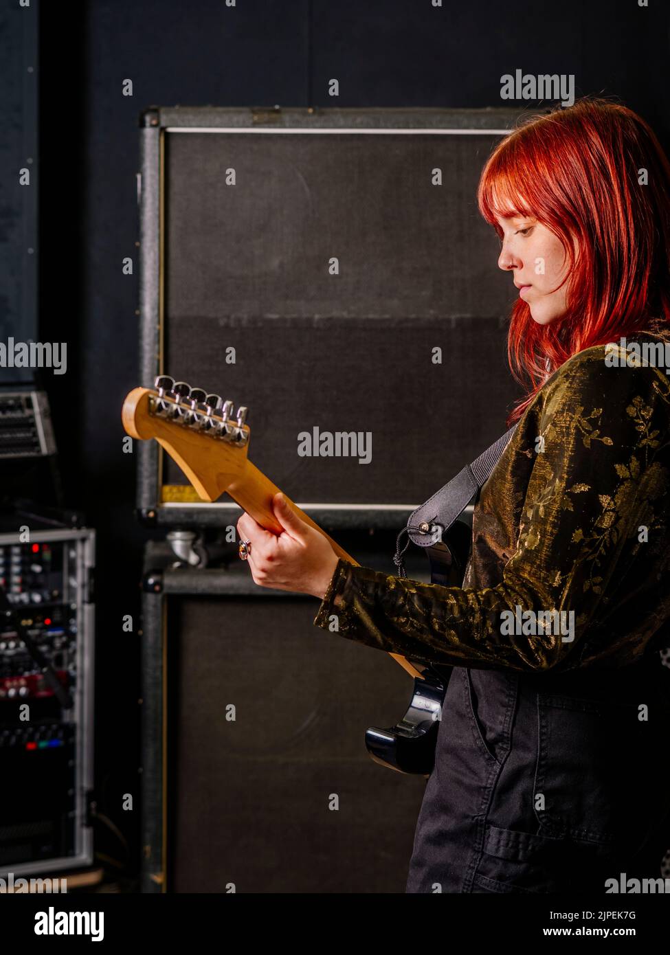 Giovane donna rossa che suona la chitarra elettrica di fronte a grandi casse. Foto Stock