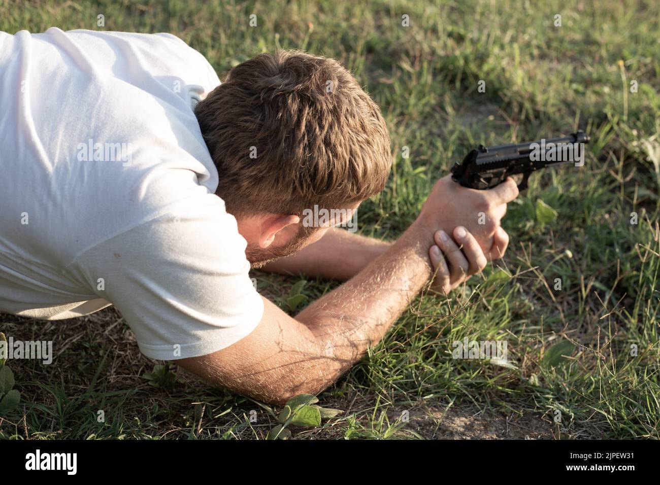 Un uomo giace sull'erba con una pistola in mano, preparandosi a sparare. Tempo libero e hobby. Foto Stock