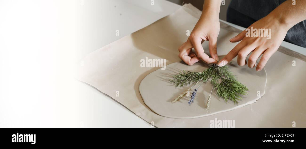 Banner Clay piatti in ceramica fatti a mano rotolati sul tavolo con piante e fiori. Vista dall'alto su ceramiche artigianali, primo piano Foto Stock