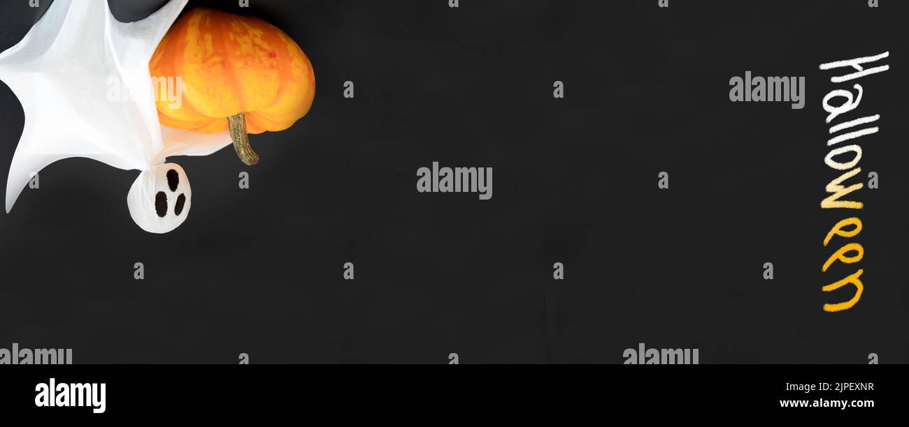 Tre fantasmi bianchi tengono zucca arancione su sfondo nero con iscrizione Halloween. Posa piatta, spazio di copia, banner, concetto di Halloween Foto Stock