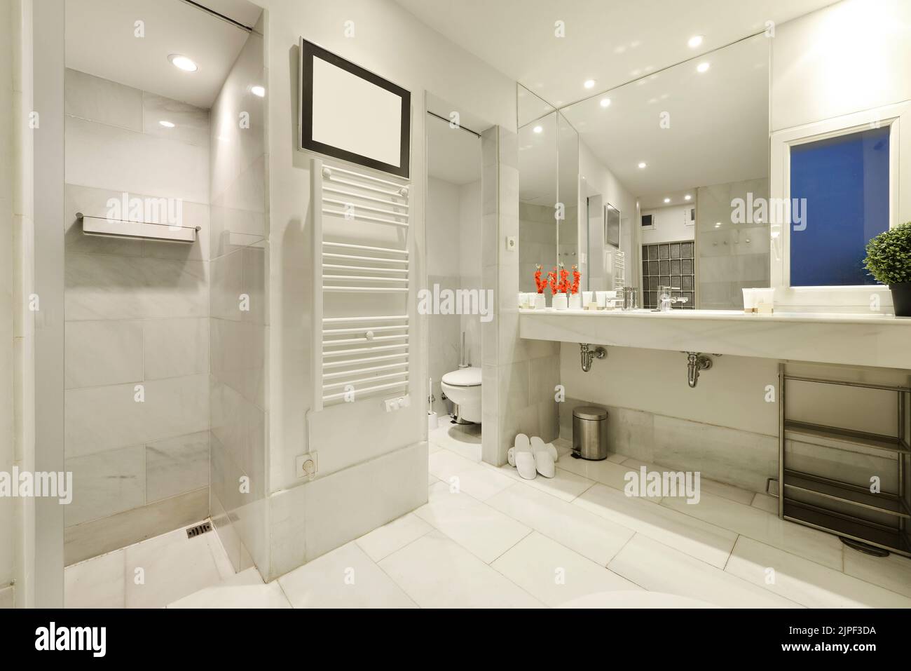 Grande bagno piastrellato con marmo bianco, piano di appoggio con due lavandini, grande specchio che copre una parete e cabine separate per doccia e wc Foto Stock