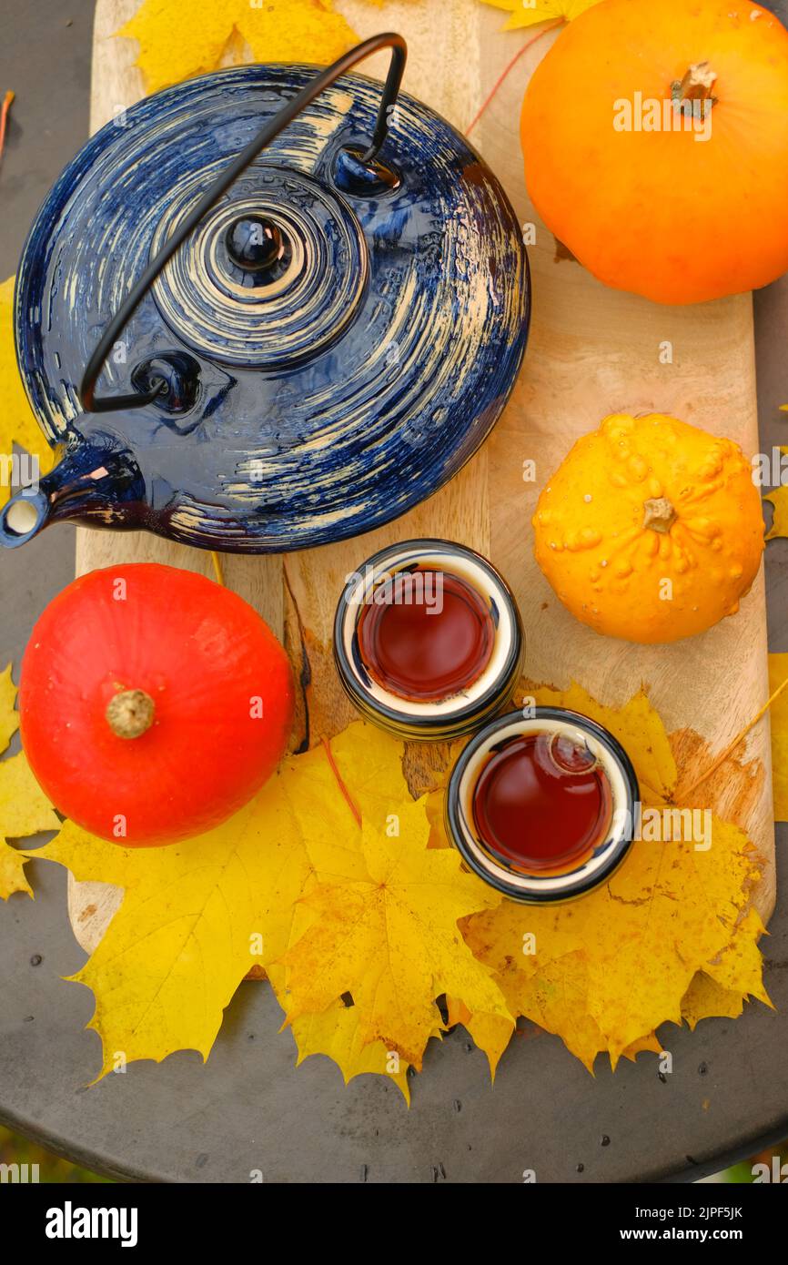 Tè bevendo.teiera e due tazze striate nel giardino in un giorno di autunno soleggiato.tazze con bevanda calda e zucche con foglie di acero. tè partito nel Foto Stock